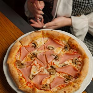 Tasty ham and mushroom pizza with a glass of red wine in a casual dining setting.